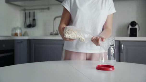 Mujer vierte harina de avena en un frasco de vidrio para el almacenamiento . — Vídeos de Stock