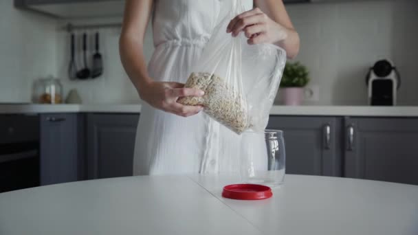 Mujer vierte harina de avena en un frasco de vidrio para el almacenamiento . — Vídeos de Stock