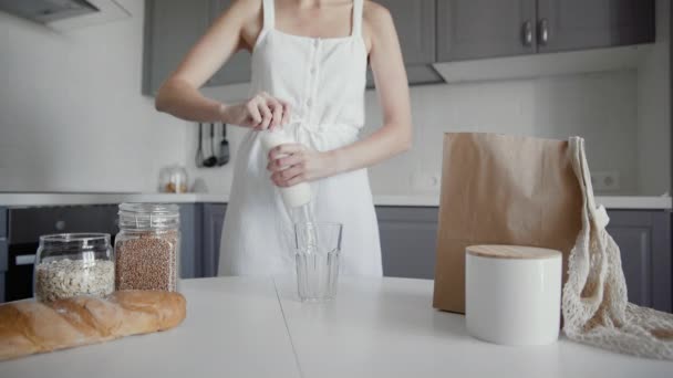 Mujer irreconocible en vestido blanco vierte la leche de la botella de la vendimia al vidrio en la mesa para el desayuno — Vídeos de Stock