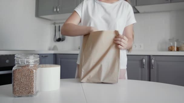 Vrouw uitpakken boodschappentas met brood, melk en sinaasappels op de keuken op houten tafel. Geen afval thuis en eco tas. Eco-winkelen. — Stockvideo