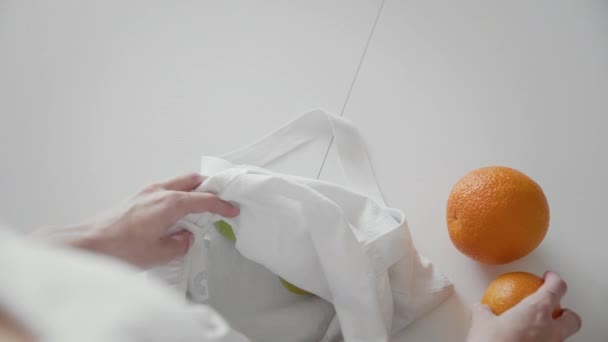 Sur la vue d'épaule de la femme déballer sac à provisions en tissu avec des pommes, des oranges et du citron sur la cuisine sur une table en bois. Zéro déchet maison et sac écologique. Eco Shopping . — Video