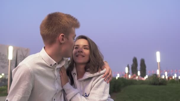 Jovem casal encantador senta-se e fala no parque de verão à noite — Vídeo de Stock