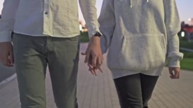 Genç çift el ele tutuşup akşam vakti yaz parkında yürüyüş yapıyor.