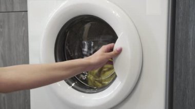 Kadın eli çamaşır makinesinden kıyafet alıyor. Çamaşır makinesi yükleniyor. Giysileri çamaşır makinesine yükleyin. Çamaşır makinesini yükle. Çamaşır yıkıyorum.
