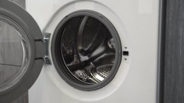 Evlilik yüzüklü bir kadın çamaşır makinesine beyaz giysiler koydu. Çamaşır makinesi yükleniyor. Giysileri çamaşır makinesine yükleyin. Çamaşır makinesini yükle. Çamaşır yıkıyorum.