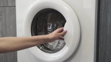 Kadın eli çamaşır makinesinden beyaz giysiler alıyor. Çamaşır makinesi yükleniyor. Giysileri çamaşır makinesine yükleyin. Çamaşır makinesini yükle. Çamaşır yıkıyorum.