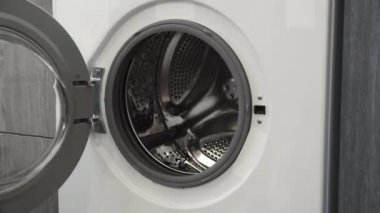 Evlilik yüzüklü bir kadın çamaşır makinesine beyaz giysiler koydu. Çamaşır makinesi yükleniyor. Giysileri çamaşır makinesine yükleyin. Çamaşır makinesini yükle. Çamaşır yıkıyorum.