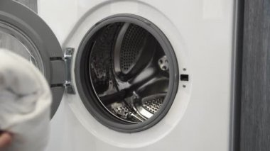 Kadın eli çamaşır makinesinden beyaz giysiler alıyor. Çamaşır makinesi yükleniyor. Giysileri çamaşır makinesine yükleyin. Çamaşır makinesini yükle. Çamaşır yıkıyorum.