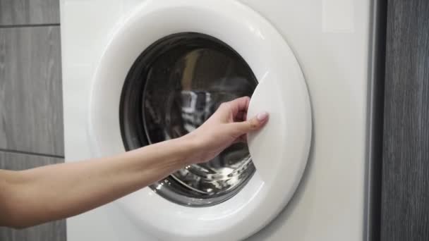 Vrouwelijke hand zet GEEL JACKET in de wasmachine. Laden wasmachine. Laad kleren in de wasmachine. Laad kleding wasmachine. Wasgoed klaarmaken — Stockvideo