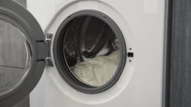 Kadın eli çamaşır makinesinden beyaz giysiler alıyor. Çamaşır makinesi yükleniyor. Giysileri çamaşır makinesine yükleyin. Çamaşır makinesini yükle. Çamaşır yıkıyorum.