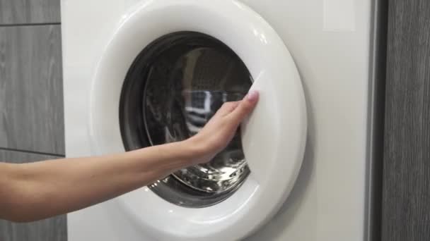 Kadın eli, soğuk giysileri çamaşır makinesine koyuyor. Çamaşır makinesi yükleniyor. Giysileri çamaşır makinesine yükleyin. Çamaşır makinesini yükle. Çamaşır yıkıyorum. — Stok video