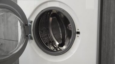 Evlilik yüzüklü bir kadın çamaşır makinesine beyaz giysiler koydu. Çamaşır makinesi yükleniyor. Giysileri çamaşır makinesine yükleyin. Çamaşır makinesini yükle. Çamaşır yıkıyorum.
