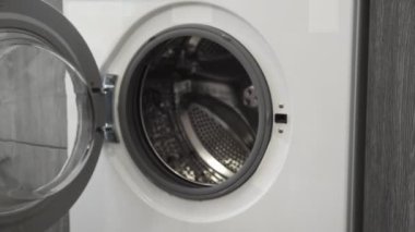 Evlilik yüzüklü kadın eli, çamaşır makinesine koyuyor. Çamaşır makinesi yükleniyor. Giysileri çamaşır makinesine yükleyin. Çamaşır makinesini yükle. Çamaşır yıkıyorum.