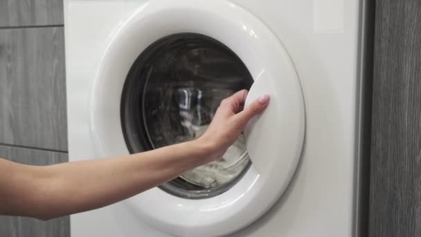 Női kéz, házas gyűrűvel, fehér ruhákat vesz ki a mosógépből. Mosógép betöltése. Ruhákat a mosógépbe. Ruha mosógép betöltése. Mosás előkészítése — Stock videók
