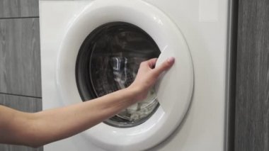 Evlilik yüzüklü bir kadın çamaşır makinesine beyaz giysiler koydu. Çamaşır makinesi yükleniyor. Giysileri çamaşır makinesine yükleyin. Çamaşır makinesini yükle. Çamaşır yıkıyorum.