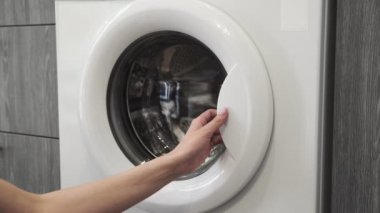 Kadın elleri çamaşır makinesine kot pantolon koydu. Çamaşır makinesi yükleniyor. Giysileri çamaşır makinesine yükleyin. Çamaşır makinesini yükle. Çamaşır yıkıyorum.