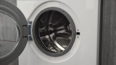 Evlilik yüzüklü bir kadın çamaşır makinesine kot pantolon koymuş. Çamaşır makinesi yükleniyor. Giysileri çamaşır makinesine yükleyin. Çamaşır makinesini yükle. Çamaşır yıkıyorum.