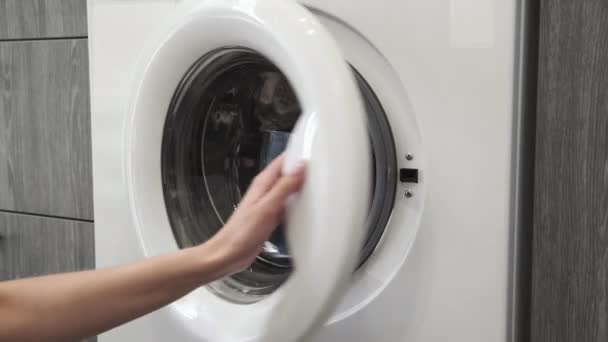 Γυναικείο χέρι παίρνει JEANS από πλυντήριο. Φόρτωση πλυντηρίου. Φόρτωσε ρούχα στο πλυντήριο. Φορτώστε ρούχα πλυντήριο ρούχων. Προετοιμασία πλυσίματος ρούχων — Αρχείο Βίντεο
