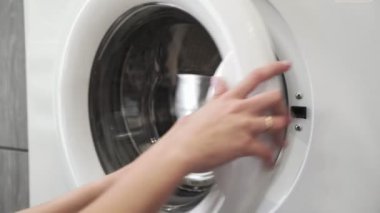 Evlilik yüzüklü bir kadın çamaşır makinesinden yeşil ayakkabıları alır. Çamaşır makinesi yükleniyor. Giysileri çamaşır makinesine yükleyin. Çamaşır makinesini yükle. Çamaşır yıkıyorum.