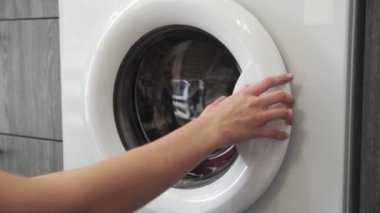 Kadın eli çamaşır makinesinden soğuk giysiler alıyor. - Ne? Çamaşır makinesi yükleniyor. Giysileri çamaşır makinesine yükleyin. Çamaşır makinesini yükle. Çamaşır yıkıyorum.