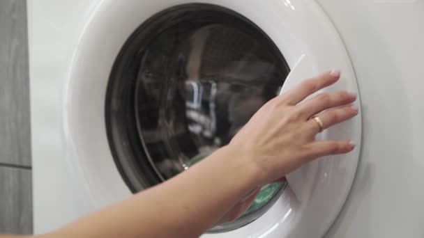 Evlilik yüzüklü bir kadın çamaşır makinesinden yeşil ayakkabıları alır. Çamaşır makinesi yükleniyor. Giysileri çamaşır makinesine yükleyin. Çamaşır makinesini yükle. Çamaşır yıkıyorum. — Stok video