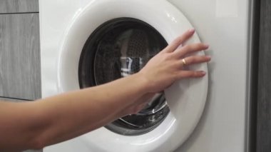 Evlilik yüzüklü kadın eli, gri süveteri çamaşır makinesine koyuyor. Çamaşır makinesi yükleniyor. Giysileri çamaşır makinesine yükleyin. Çamaşır makinesini yükle. Çamaşır yıkıyorum.