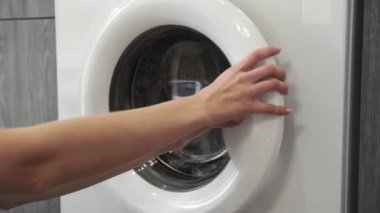 Kadın eli çamaşır makinesinden gri süveteri alır. Çamaşır makinesi yükleniyor. Giysileri çamaşır makinesine yükleyin. Çamaşır makinesini yükle. Çamaşır yıkıyorum.