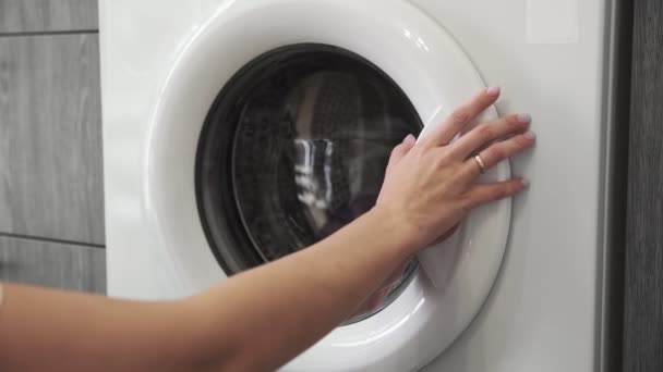 La mano femenina con anillo casado toma PURPLE CloTHES de la lavadora. Cargando lavadora. Carga la ropa a la lavadora. Carga la ropa lavadora. Preparación del lavado de ropa — Vídeos de Stock