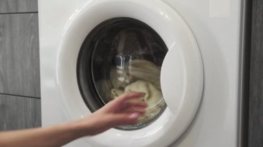 Kadın eli çamaşır makinesinden beyaz süveteri alır. Çamaşır makinesi yükleniyor. Giysileri çamaşır makinesine yükleyin. Çamaşır makinesini yükle. Çamaşır yıkıyorum.