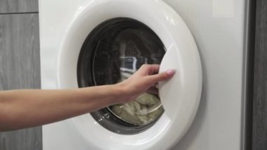 Kadın eli çamaşır makinesinden iki beyaz süveter alır. Çamaşır makinesi yükleniyor. Giysileri çamaşır makinesine yükleyin. Çamaşır makinesini yükle. Çamaşır yıkıyorum.