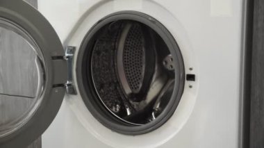 Evlilik yüzüklü bir kadın çamaşır makinesine iki beyaz süveter koyar. Çamaşır makinesi yükleniyor. Giysileri çamaşır makinesine yükleyin. Çamaşır makinesini yükle. Çamaşır yıkıyorum.