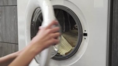 Evlilik yüzüklü bir kadın çamaşır makinesinden iki beyaz süveter alır. Çamaşır makinesi yükleniyor. Giysileri çamaşır makinesine yükleyin. Çamaşır makinesini yükle. Çamaşır yıkıyorum.