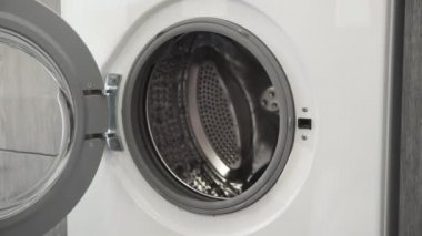 Evlilik yüzüklü bir kadın çamaşır makinesinden GRAY KNITED HATS alır. Çamaşır makinesi yükleniyor. Giysileri çamaşır makinesine yükleyin. Çamaşır makinesini yükle. Çamaşır yıkıyorum.