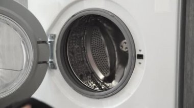 Evlilik yüzüklü bir kadın çamaşır makinesine siyah giysiler koydu. Çamaşır makinesi yükleniyor. Giysileri çamaşır makinesine yükleyin. Çamaşır makinesini yükle. Çamaşır yıkıyorum.
