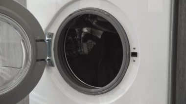 Evlilik yüzüklü bir kadın çamaşır makinesinden beyaz giysiler alır. Çamaşır makinesi yükleniyor. Giysileri çamaşır makinesine yükleyin. Çamaşır makinesini yükle. Çamaşır yıkıyorum.