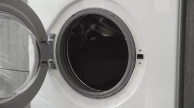 Kadın eli çamaşır makinesinden beyaz giysiler alıyor. Çamaşır makinesi yükleniyor. Giysileri çamaşır makinesine yükleyin. Çamaşır makinesini yükle. Çamaşır yıkıyorum.