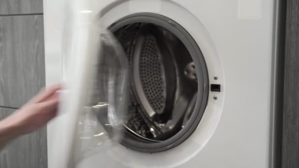 Female hand with married ring puts GRAY KNITTED HATS in laundry machine. Loading washing machine. Load clothes to washer machine. Load clothes laundry washing machine. Preparing laundry washing — Stock Video