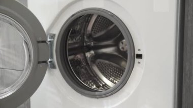 Evlilik yüzüklü bir kadın çamaşır makinesine beyaz ve kırmızı giysiler koyar. Çamaşır makinesi yükleniyor. Giysileri çamaşır makinesine yükleyin. Çamaşır makinesini yükle. Çamaşır yıkıyorum.