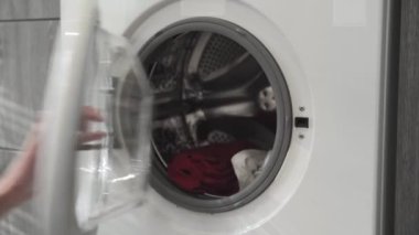 Evlilik yüzüklü bir kadın çamaşır makinesinden beyaz ve kırmızı giysiler alır. Çamaşır makinesi yükleniyor. Giysileri çamaşır makinesine yükleyin. Çamaşır makinesini yükle. Çamaşır yıkıyorum.