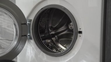 Evlilik yüzüklü kadın eli siyah elbiseleri çamaşır makinesine koyuyor. Çamaşır makinesi yükleniyor. Giysileri çamaşır makinesine yükleyin. Çamaşır makinesini yükle. Çamaşır yıkıyorum.