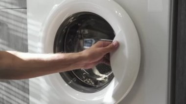 Evlilik yüzüklü bir erkek, siyah giysileri çamaşır makinesine koyar. Çamaşır makinesi yükleniyor. Giysileri çamaşır makinesine yükleyin. Çamaşır makinesini yükle. Çamaşır yıkıyorum.
