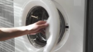 Evlilik yüzüklü bir erkek, kot pantolonları çamaşır makinesine koyuyor. Çamaşır makinesi yükleniyor. Giysileri çamaşır makinesine yükleyin. Çamaşır makinesini yükle. Çamaşır yıkıyorum.
