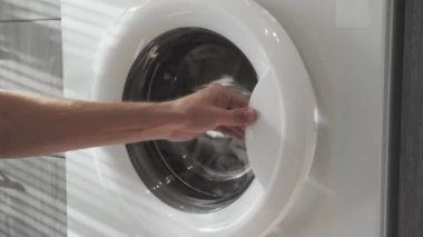 Erkek eli gri giysileri çamaşır makinesine koyuyor. Çamaşır makinesi yükleniyor. Giysileri çamaşır makinesine yükleyin. Çamaşır makinesini yükle. Çamaşır yıkıyorum.