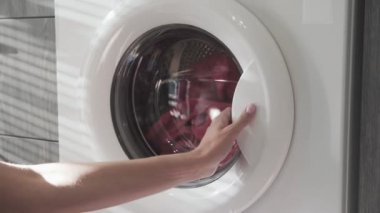 Kadın eli, çamaşır makinesinden pembe giysiler alıyor. Çamaşır makinesi yükleniyor. Giysileri çamaşır makinesine yükleyin. Çamaşır makinesini yükle. Çamaşır yıkıyorum.