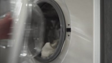 Evlilik yüzüklü bir kadın çamaşır makinesinden beyaz giysiler alır. Çamaşır makinesi yükleniyor. Giysileri çamaşır makinesine yükleyin. Çamaşır makinesini yükle. Çamaşır yıkıyorum.