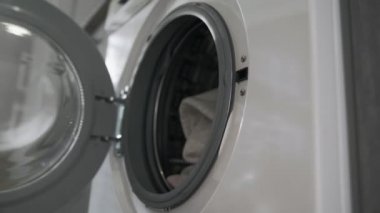 Evlilik yüzüklü bir kadın çamaşır makinesinden gri giysiler alır. Çamaşır makinesi yükleniyor. Giysileri çamaşır makinesine yükleyin. Çamaşır makinesini yükle. Çamaşır yıkıyorum.