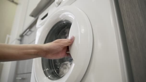여자들은 빨래 기계를 열고 흰 옷을 입는다. 화물 세탁기. 세탁기에 옷을 싣는다. 빨래 빨래 세탁기를 싣는 일 — 비디오