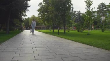 Kadın elinde sebzelerle pamuk ağıyla alışveriş çantası tutuyor ve yaz parkında yürüyor.