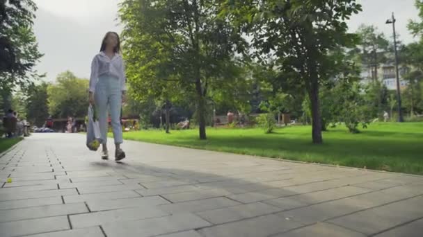 Όμορφη νεαρή γυναίκα κρατά βαμβακερή τσάντα ψώνια με λαχανικά και βόλτες στο πάρκο το καλοκαίρι — Αρχείο Βίντεο