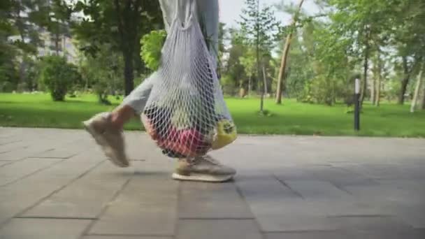 Felismerhetetlen nő tartja pamut háló bevásárló táska zöldségek és séták a nyári parkban — Stock videók